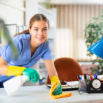 Weibliche Reinigungskraft, die einen Büroschreibtisch mit Lappen und Reinigungsmittel putzt