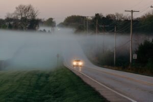Auto auf Straße im Nebel und eingeschaltetem Licht