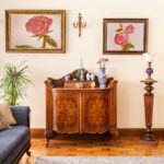 Eine antike Kommode mit Porzellandekorationen und Gemälde mit Rosen und blauem Sofa in einem Wohnzimmer