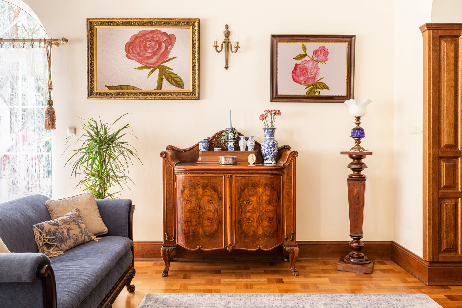 Eine antike Kommode mit Porzellandekorationen und Gemälde mit Rosen und blauem Sofa in einem Wohnzimmer
