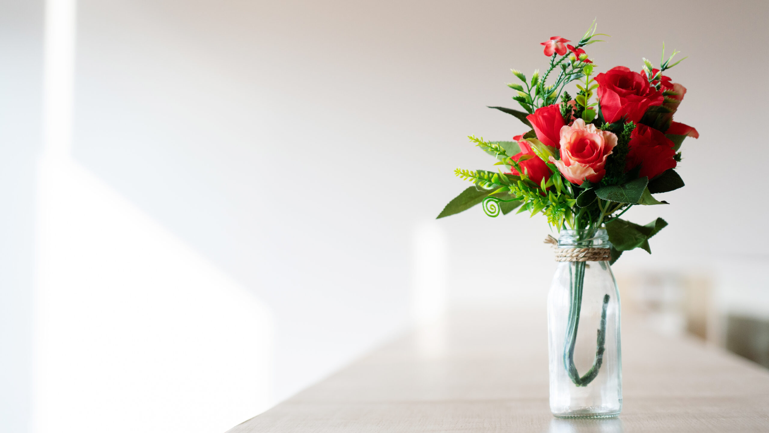 Blumenstrauß aus roten Plastikrosen in einer Glasflasche auf einem Holztisch