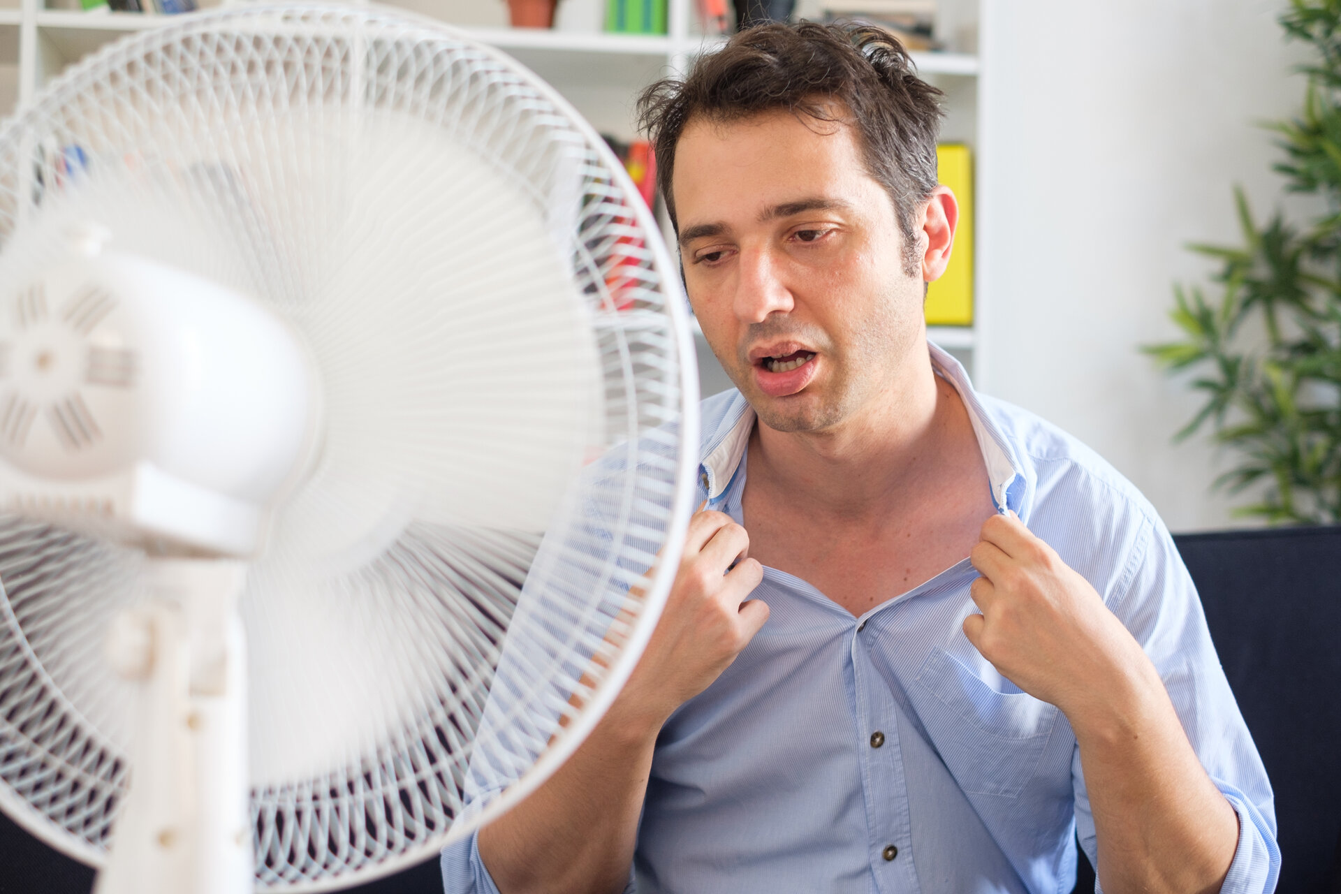 Mann schwitzt und versucht sich vor Ventilator abzukühlen.